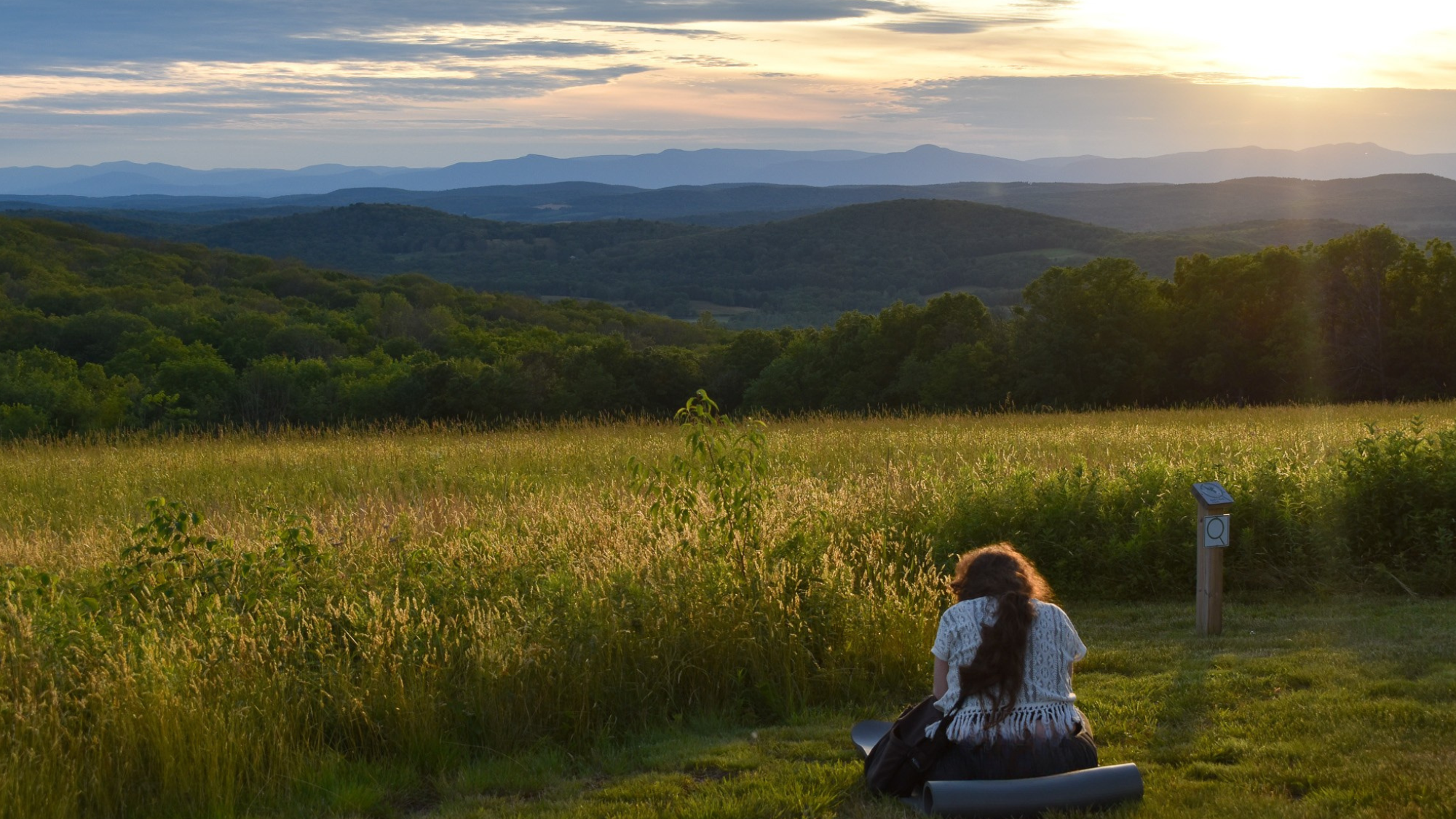 Individual sitting on yoga mat on grass at Overmountain, with a mountain view in the distance Used for promotion of mindfulness meditation